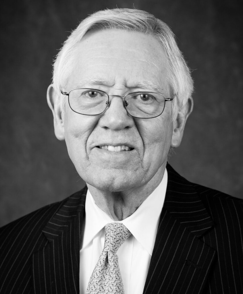 A black and white headshot of Jim Millerman, who passed in 2016 after a battle with cancer. Millerman is wearing a dark suit jacket with a light dress shirt and colored tie. He smiling for the camera.